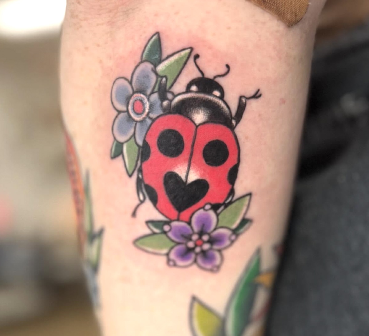 Traditional ladybug with heart spots and flowers — bold bright-color tattoo by Cat Bernardy